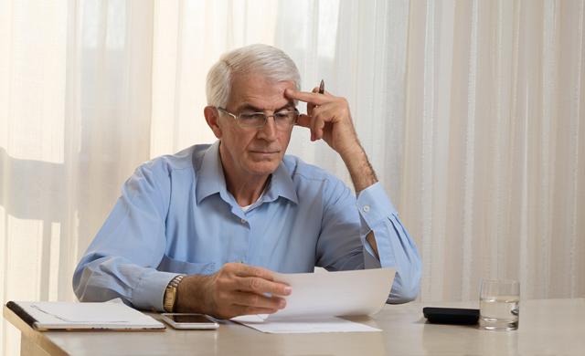 older man at desk concentrating on paperwork